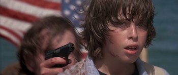 Movie still from “The Island” (1980), directed by Michael Ritchie – Two young people with guns in front of an american flag; Close Up shot, Over the shoulder angle