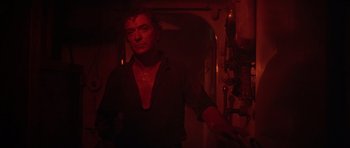 Movie still from “The Island” (1980), directed by Michael Ritchie – A man standing in a dark room with a red light; Medium shot, Low angle
