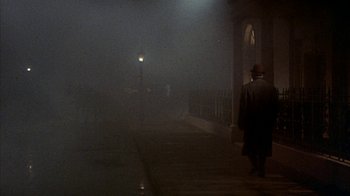 Movie still from “The Island at the Top of the World” (1974), directed by Robert Stevenson – A man walking down a sidewalk in the fog; Wide shot, High angle