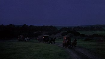 Movie still from “The Island at the Top of the World” (1974), directed by Robert Stevenson – A group of people riding in a carriage on a dirt road; Extreme Wide shot, High angle