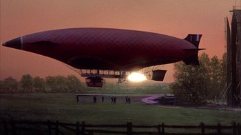Movie still from “The Island at the Top of the World” (1974), directed by Robert Stevenson – A group of people standing in front of an airship in a field; Extreme Wide shot, Low angle