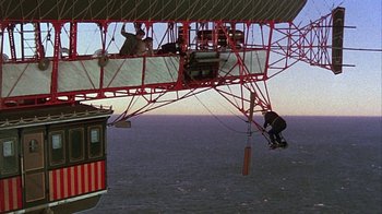 Movie still from “The Island at the Top of the World” (1974), directed by Robert Stevenson – A man hanging from the side of a red and white boat; Extreme Wide shot, Low angle