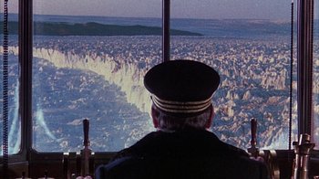 Movie still from “The Island at the Top of the World” (1974), directed by Robert Stevenson – An older man in a uniform looking out a window; Wide shot, High angle