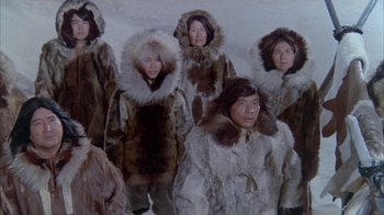 Movie still from “The Island at the Top of the World” (1974), directed by Robert Stevenson – A group of people in fur coats standing next to each other in the snow; Wide shot, High angle
