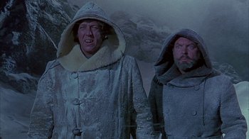 Movie still from “The Island at the Top of the World” (1974), directed by Robert Stevenson – Two men are standing in the snow wearing coats; Medium shot, Low angle