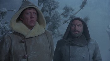 Movie still from “The Island at the Top of the World” (1974), directed by Robert Stevenson – Two men are standing in the snow wearing coats and hoods; Medium shot, Low angle