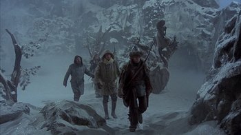 Movie still from “The Island at the Top of the World” (1974), directed by Robert Stevenson – A group of people walking through a snowy forest; Wide shot, Low angle