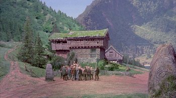 Movie still from “The Island at the Top of the World” (1974), directed by Robert Stevenson – A group of people standing in front of a house; Extreme Wide shot, High angle