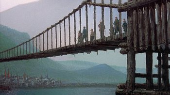 Movie still from “The Island at the Top of the World” (1974), directed by Robert Stevenson – A group of people walking across a wooden bridge over a river; Extreme Wide shot, Low angle