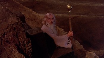 Movie still from “The Island at the Top of the World” (1974), directed by Robert Stevenson – An old man with a long white beard holding a staff; Medium shot, High angle