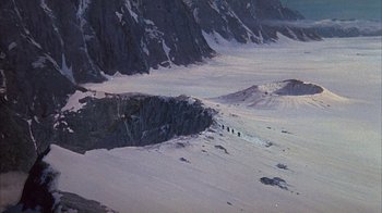 Movie still from “The Island at the Top of the World” (1974), directed by Robert Stevenson – A group of people walking across a snow covered slope; Extreme Wide shot, High angle