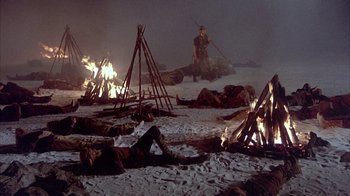Movie still from “The Island at the Top of the World” (1974), directed by Robert Stevenson – A group of people laying in the snow next to burning trees; Wide shot, High angle