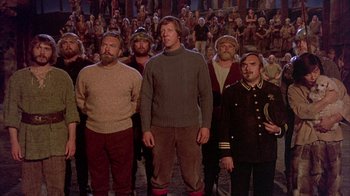 Movie still from “The Island at the Top of the World” (1974), directed by Robert Stevenson – A group of men standing in front of a crowd; Wide shot, High angle