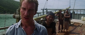 Movie still from “The Island of Dr. Moreau” (1996), directed by Richard Stanley – A man standing next to two other men on a boat; Close Up shot, Low angle
