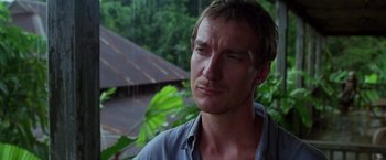 Movie still from “The Island of Dr. Moreau” (1996), directed by Richard Stanley – A person wearing a blue shirt near trees; Close Up shot, Low angle