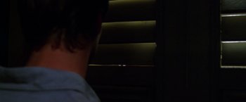 Movie still from “The Island of Dr. Moreau” (1996), directed by Richard Stanley – A man standing in front of a window with blinds open; Close Up shot, Over the shoulder angle