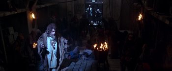 Movie still from “The Island of Dr. Moreau” (1996), directed by Richard Stanley – A group of people sitting around a fire pit; Wide shot, High angle