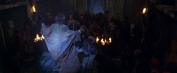 Movie still from “The Island of Dr. Moreau” (1996), directed by Richard Stanley – A group of people sitting around a fire pit; Wide shot, High angle