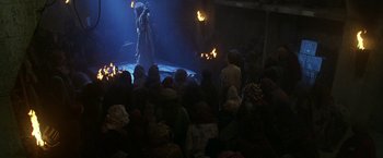 Movie still from “The Island of Dr. Moreau” (1996), directed by Richard Stanley – A crowd of people watching a fire show on a stage; Wide shot, High angle