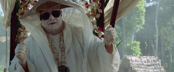 Movie still from “The Island of Dr. Moreau” (1996), directed by Richard Stanley – An old man in a white robe holding a flower; Medium shot, Low angle