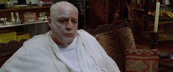 Movie still from “The Island of Dr. Moreau” (1996), directed by Richard Stanley – An older man sitting on a couch wearing a towel; Close Up shot, High angle