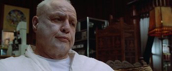 Movie still from “The Island of Dr. Moreau” (1996), directed by Richard Stanley – An older man sitting in front of a wooden chair; Close Up shot, Low angle