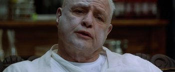 Movie still from “The Island of Dr. Moreau” (1996), directed by Richard Stanley – An older man with a shaved head and a white shirt; Close Up shot, Low angle
