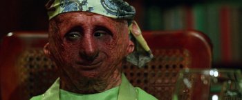 Movie still from “The Island of Dr. Moreau” (1996), directed by Richard Stanley – A man with a green shirt is wearing a hat; Close Up shot, High angle