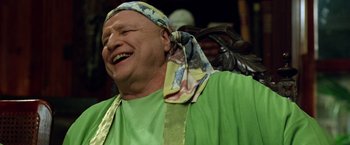 Movie still from “The Island of Dr. Moreau” (1996), directed by Richard Stanley – An older man wearing a green shirt and a colorful head scarf; Close Up shot, Over the shoulder angle