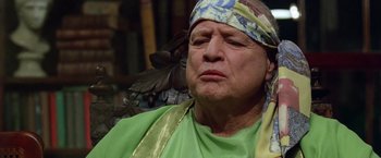 Movie still from “The Island of Dr. Moreau” (1996), directed by Richard Stanley – An older man wearing a green shirt with a bird on his head; Close Up shot, Low angle