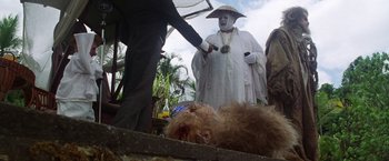 Movie still from “The Island of Dr. Moreau” (1996), directed by Richard Stanley – A man in a white robe standing next to a dead animal; Medium shot, Low angle