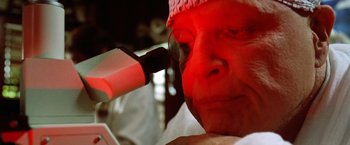 Movie still from “The Island of Dr. Moreau” (1996), directed by Richard Stanley – An older man looking through a magnifying glass; Extreme Close Up shot, Low angle