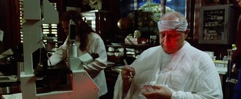 Movie still from “The Island of Dr. Moreau” (1996), directed by Richard Stanley – A man in a white lab coat is holding something in his hand; Medium shot, Over the shoulder angle