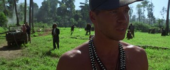 Movie still from “The Island of Dr. Moreau” (1996), directed by Richard Stanley – A group of people standing on a lush green field; Close Up shot, Over the shoulder angle