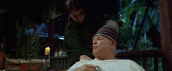 Movie still from “The Island of Dr. Moreau” (1996), directed by Richard Stanley – An older man and a younger woman are sitting in a chair; Medium shot, Low angle