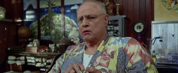 Movie still from “The Island of Dr. Moreau” (1996), directed by Richard Stanley – An older man wearing a colorful shirt and a ring in his hand; Close Up shot, Low angle