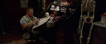 Movie still from “The Island of Dr. Moreau” (1996), directed by Richard Stanley – A man sitting in a chair with a skull on his lap; Wide shot, Low angle