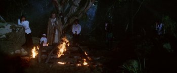 Movie still from “The Island of Dr. Moreau” (1996), directed by Richard Stanley – A group of people standing around a fire; Wide shot, Low angle