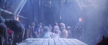 Movie still from “The Island of Dr. Moreau” (1996), directed by Richard Stanley – A group of people sitting around a building; Wide shot, Low angle