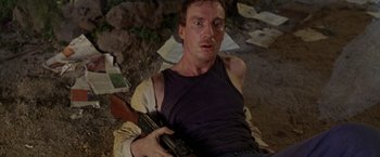 Movie still from “The Island of Dr. Moreau” (1996), directed by Richard Stanley – A man holding a gun while sitting on the ground; Medium shot, High angle