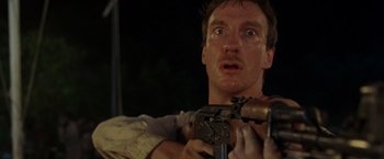 Movie still from “The Island of Dr. Moreau” (1996), directed by Richard Stanley – A person holding a machine gun; Close Up shot, Low angle