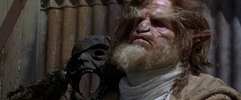 Movie still from “The Island of Dr. Moreau” (1996), directed by Richard Stanley – An old man with a beard and a wooden mask; Close Up shot, Low angle
