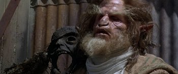 Movie still from “The Island of Dr. Moreau” (1996), directed by Richard Stanley – An old man with a beard and a wooden mask; Close Up shot, Low angle