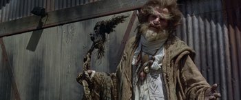 Movie still from “The Island of Dr. Moreau” (1996), directed by Richard Stanley – A man with a beard and a long beard holding an axe; Medium shot, Low angle