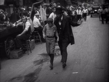 Movie still from “The Jazz Singer” (1927), directed by Alan Crosland – A man walking down a street with a man in a hat; Wide shot, High angle