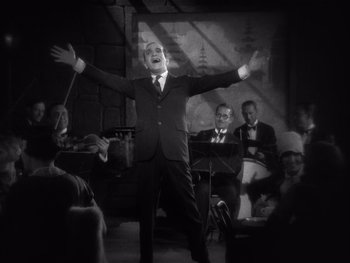 Movie still from “The Jazz Singer” (1927), directed by Alan Crosland – A black and white photo of a man in a suit singing; Medium shot, Low angle