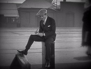 Movie still from “The Jazz Singer” (1927), directed by Alan Crosland – A man sitting on top of a piece of luggage writing; Wide shot, High angle