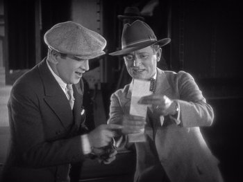 Movie still from “The Jazz Singer” (1927), directed by Alan Crosland – Two men in suits and hats are looking at a piece of paper; Medium shot, High angle