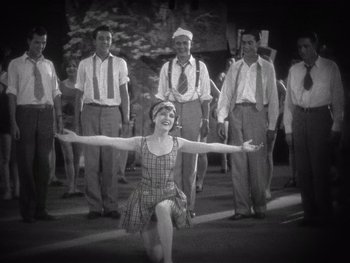 Movie still from “The Jazz Singer” (1927), directed by Alan Crosland – An old photo of a woman in a plaid dress with a group of men; Wide shot, Low angle