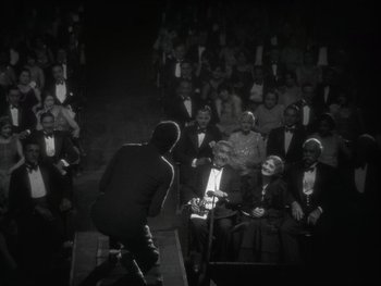 Movie still from “The Jazz Singer” (1927), directed by Alan Crosland – An audience watching a man on a stage singing; Wide shot, High angle